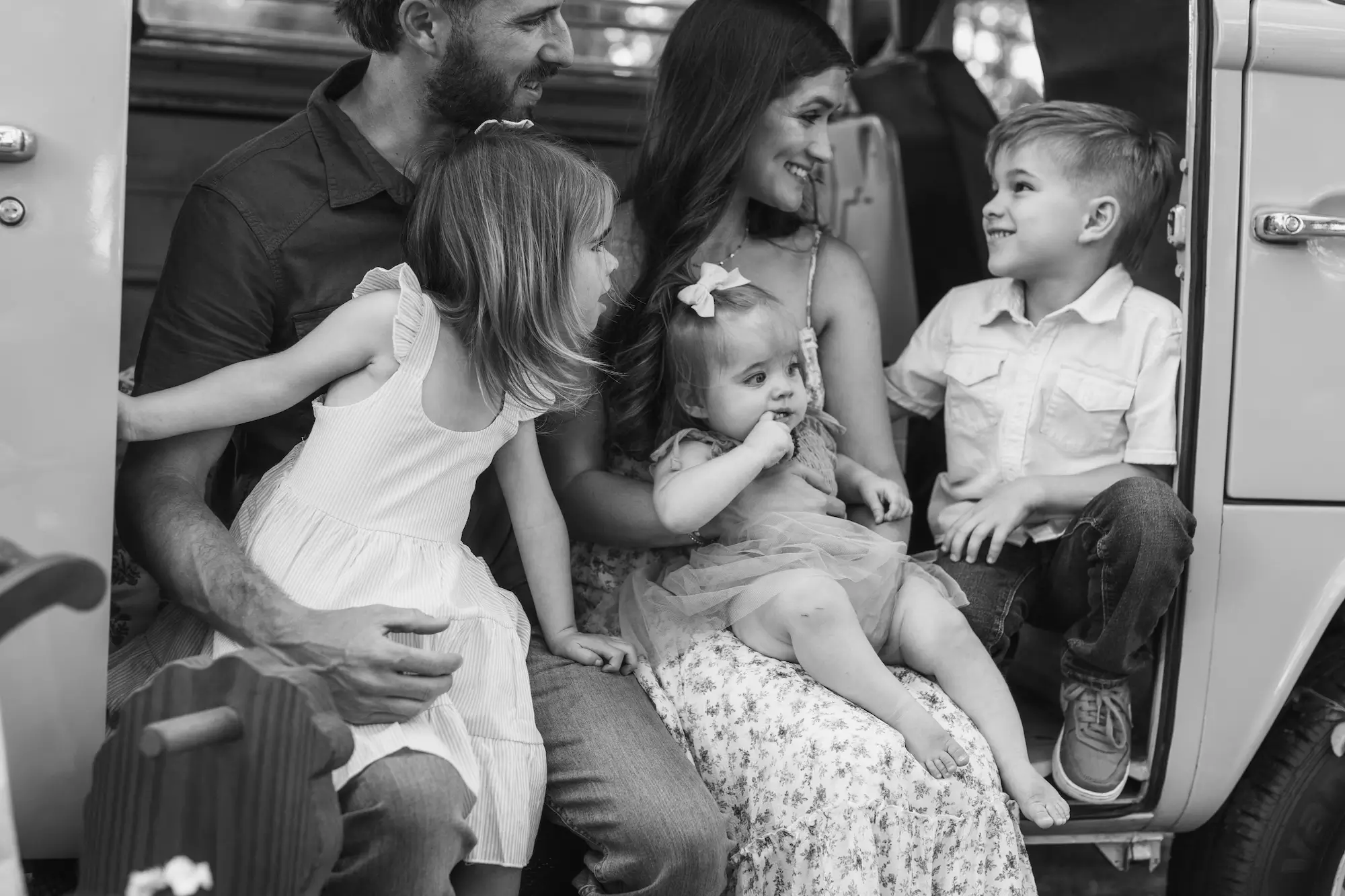 Family of five laughing together in the open door of a vintage van during a candid family photography session
